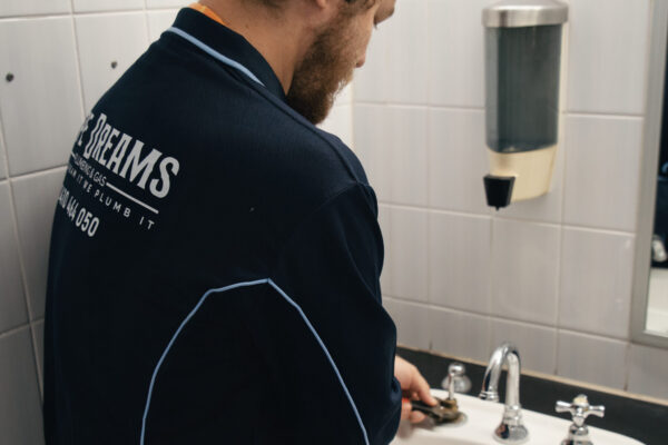 Plumber tightening taps in an office bathroom for maintenance plumbing
