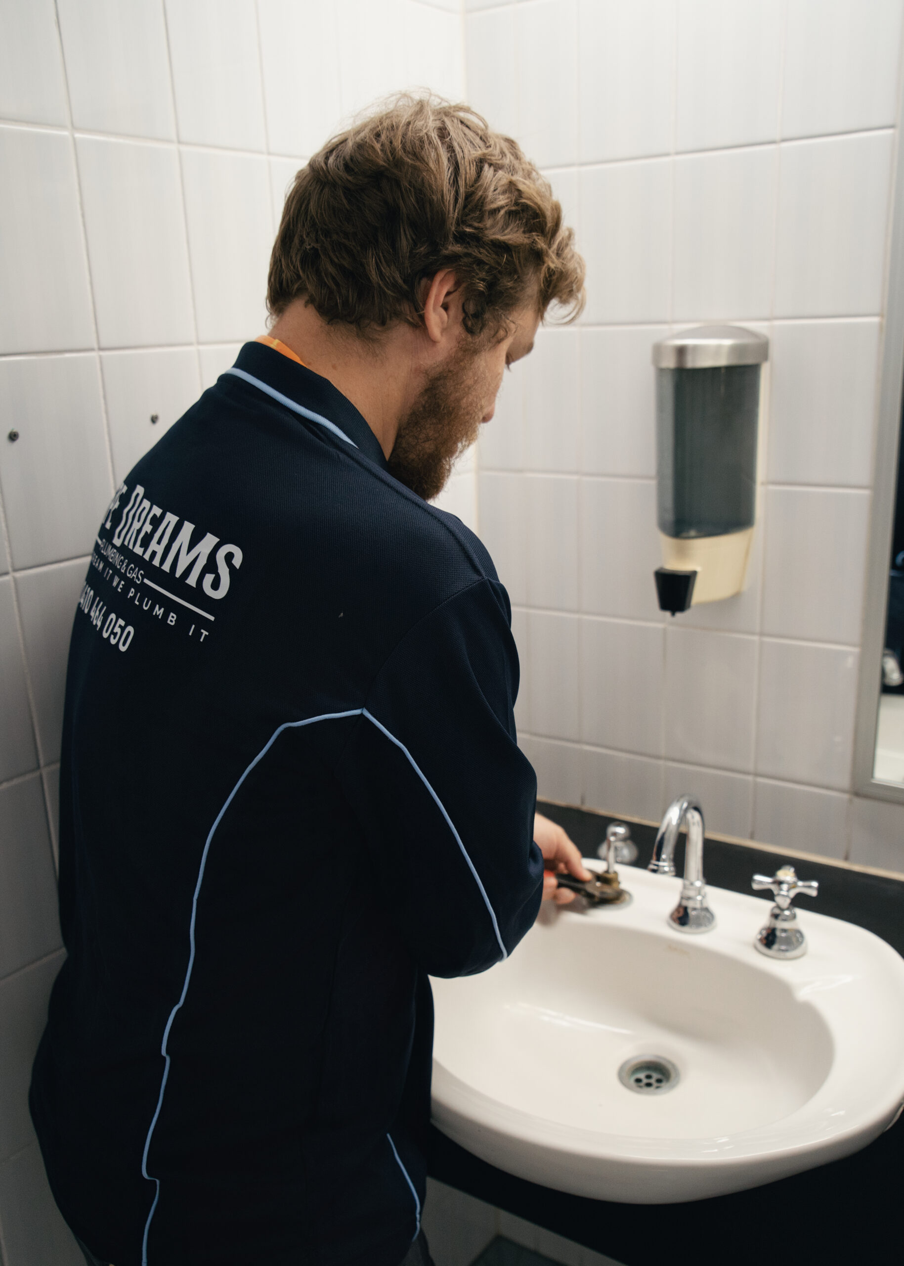 Plumber tightening taps in an office bathroom for maintenance plumbing