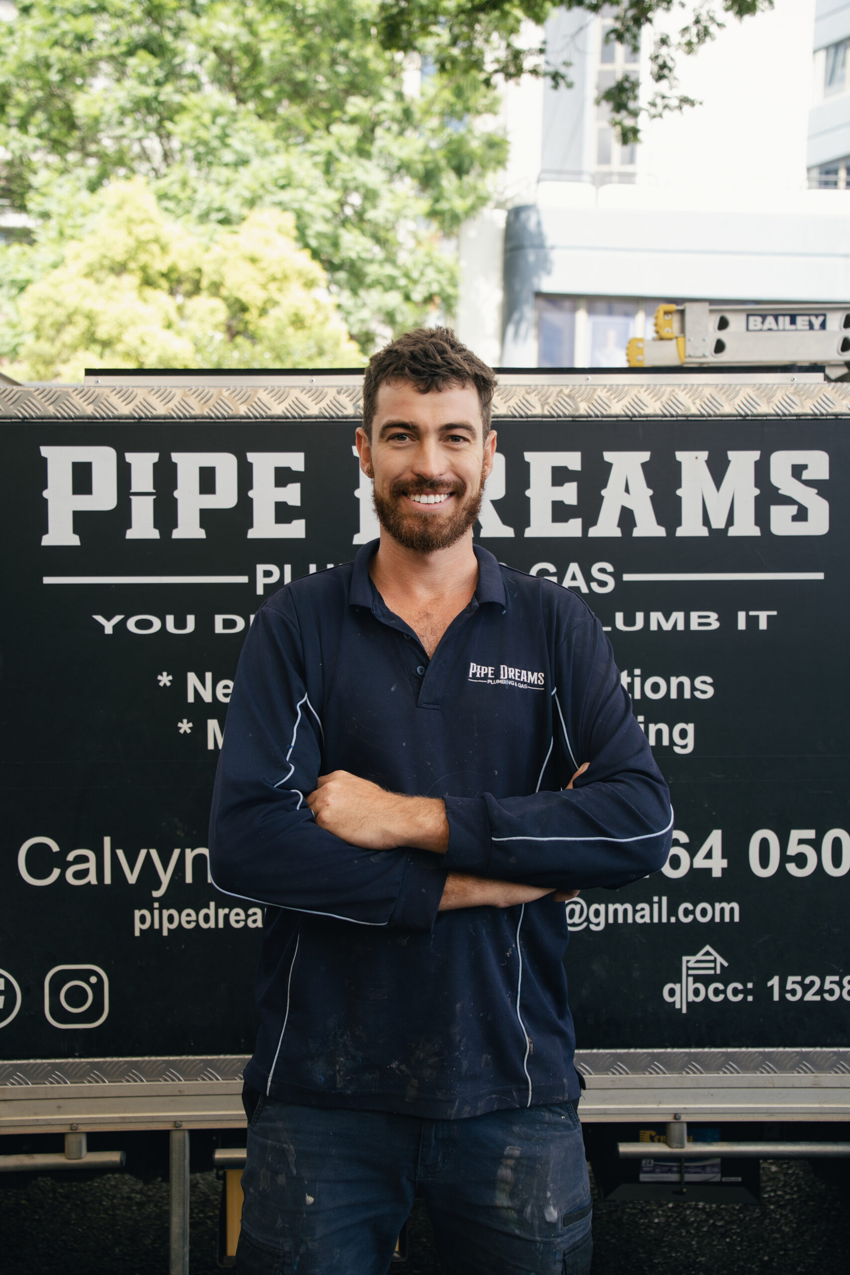 Handsome plumber smiling with arms folded against home page Pipe Dreams work truck
