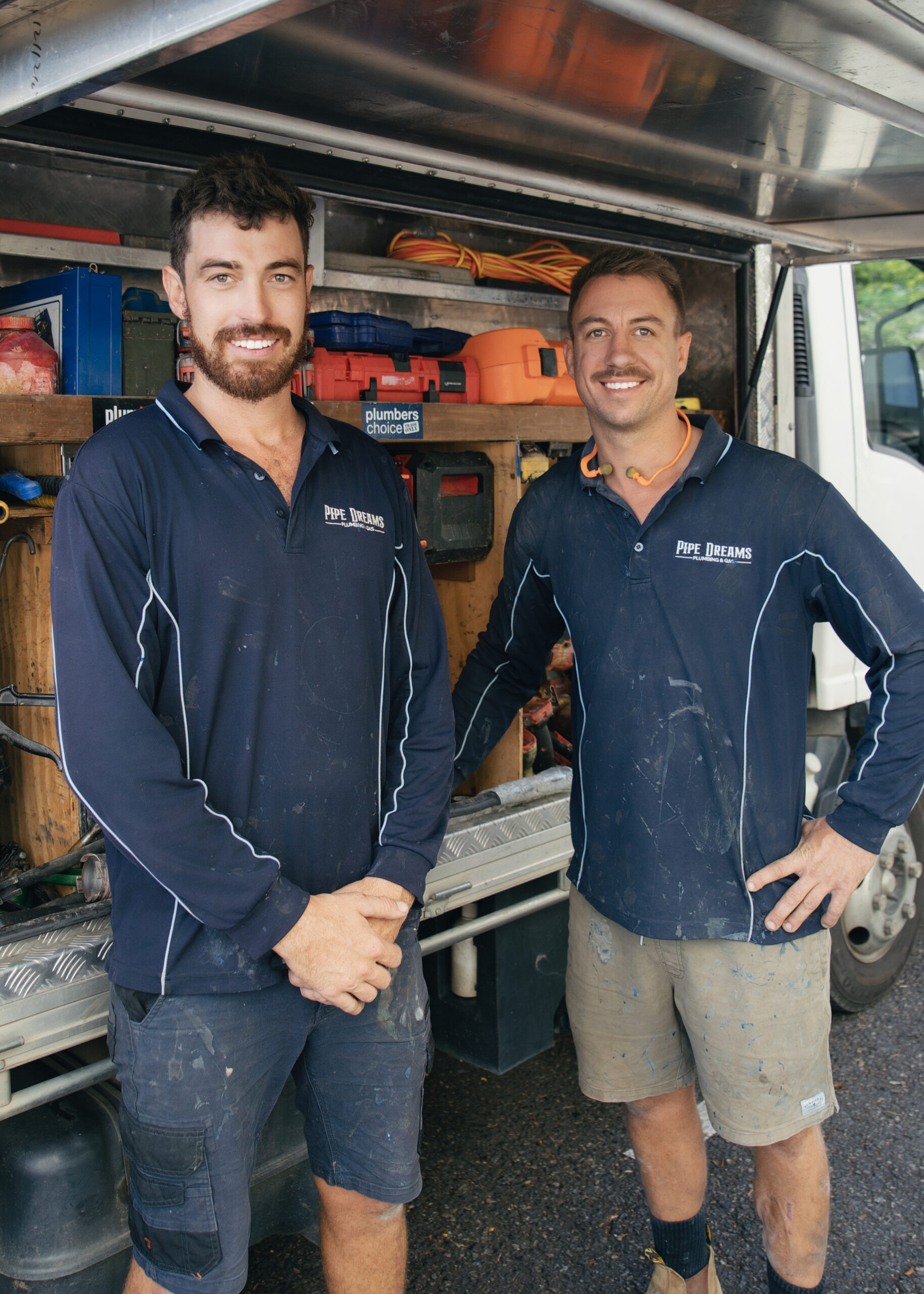Two handsome plumber standing and leaning against pipe dreams plumbing truck welcoming customers to contact us